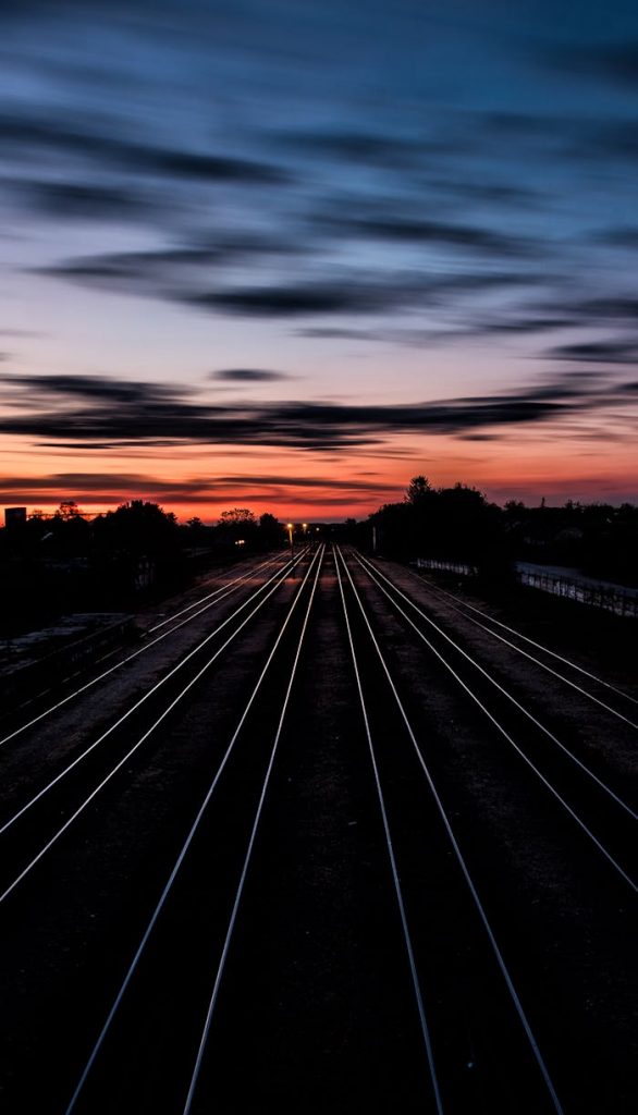 Long railway tracks stretching into the horizon under a dramatic twilight sky.